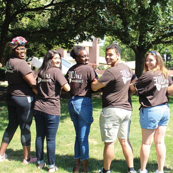 Locked arm in arm, three students with "Let Love Overwhelm Fear" on the back of their t-shirt turn to look at the camera