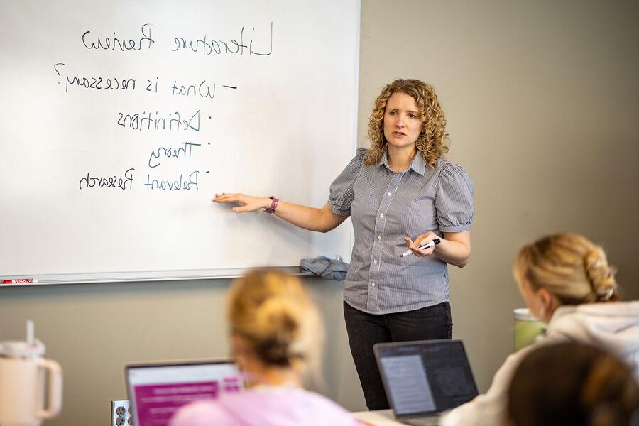 Chelsea Klinkebiel teaching in front of a class pointing towards a white board.